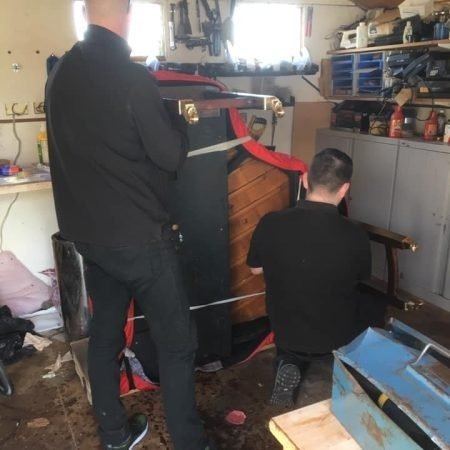 Piano movers Sussex team carrying an upright piano with moving straps